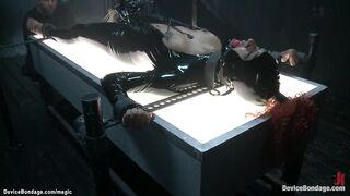 Ginger black serf Daisy Ducati in latex costume shacled laid on illuminating table and snatch bibed then clamped and booty hooked on device servitude